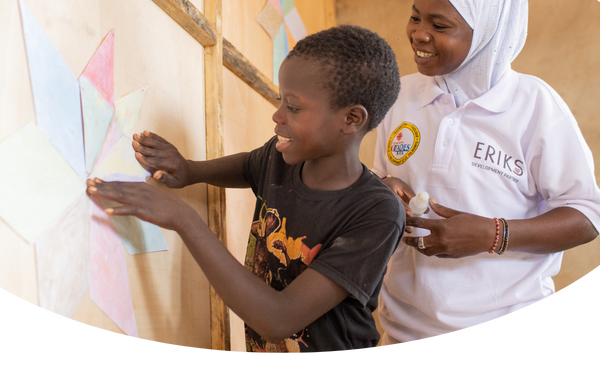 En lärare assisterar en elev med att sätta upp pappersstjärnor på väggarrna i en skola i Burkina faso.